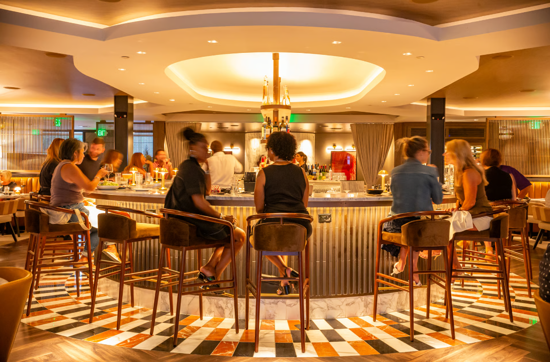 An image of restaurant guests seated at a circular bar, chatting with one another.