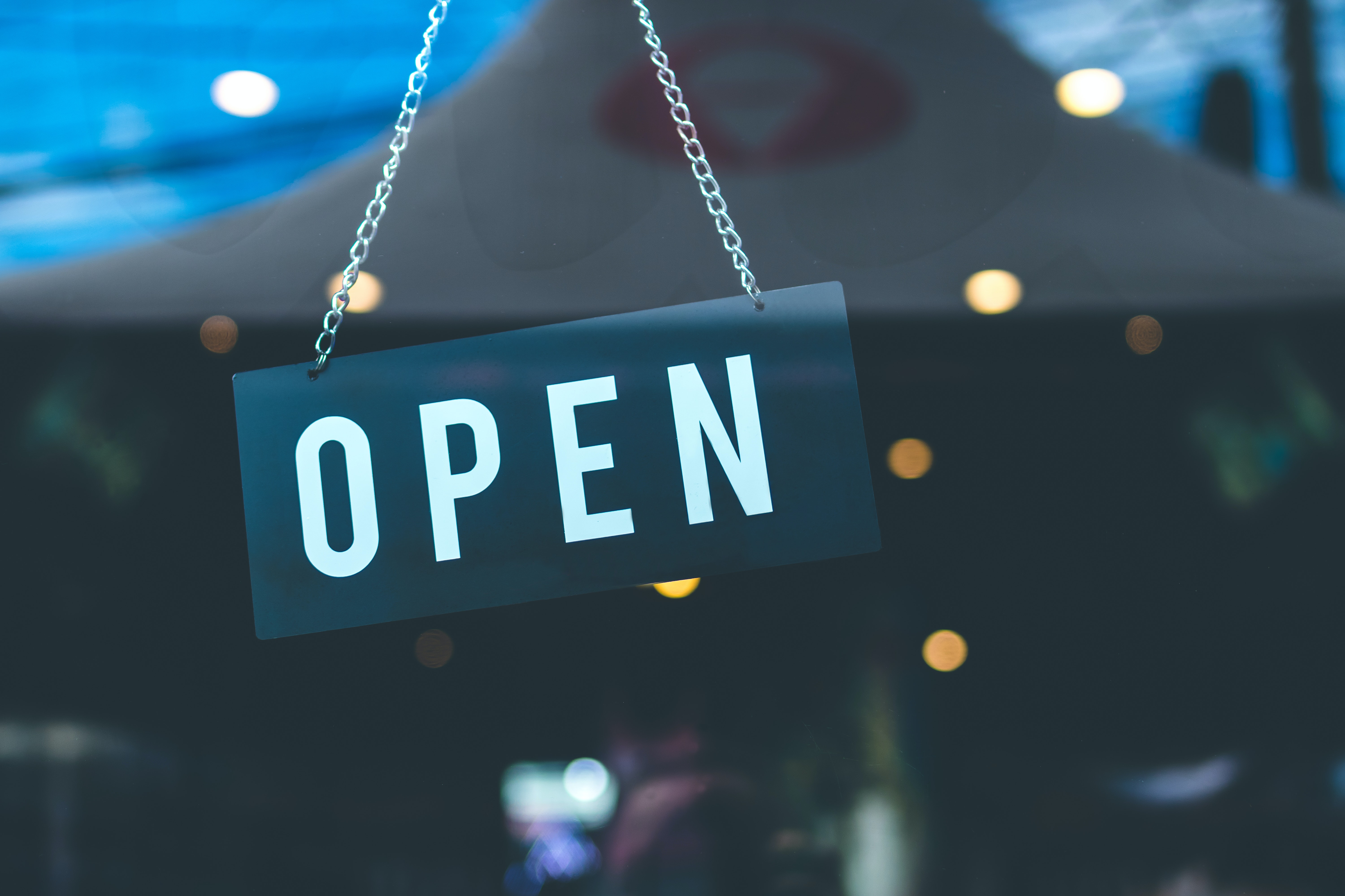 Decorative Image with a black sign printed with the word OPEN in white hanging on a chain captured through a windowpane.