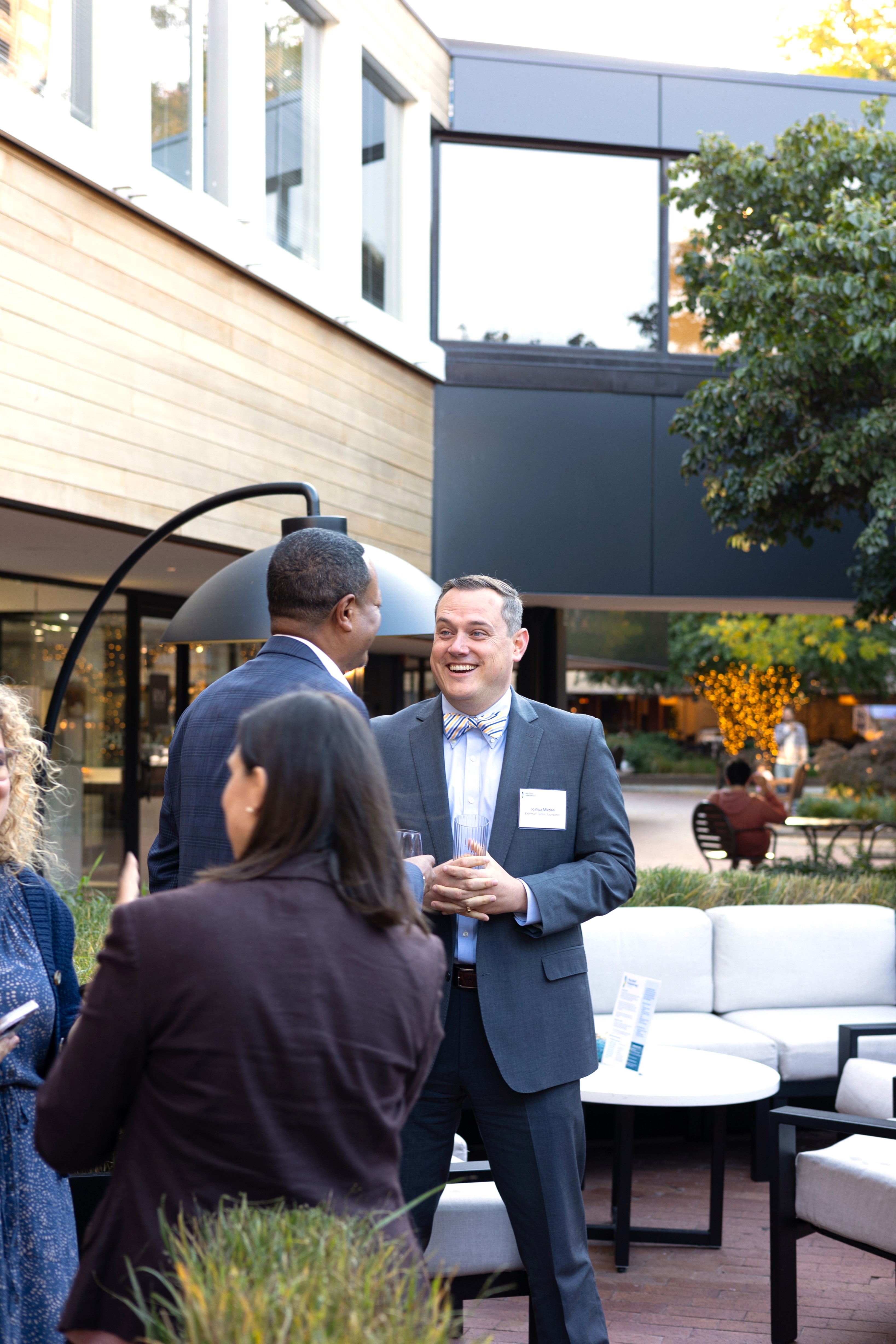 Image of two people in suits conversing and smiling at one another on an outdoor patio.