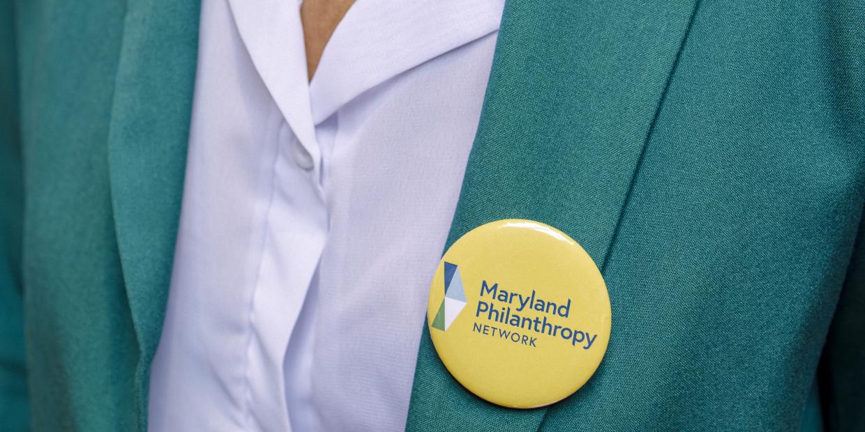 A yellow pin-on button with MPN's logo adorns someone's teal blazer.