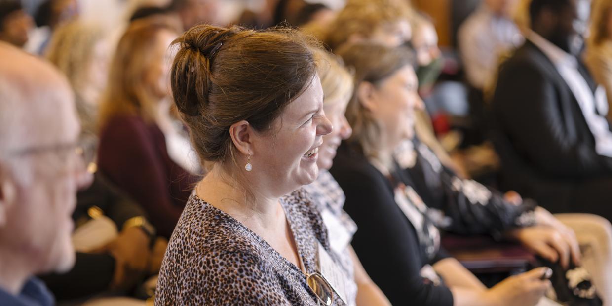 Person in auditorium style seating is smiling at the speaker.