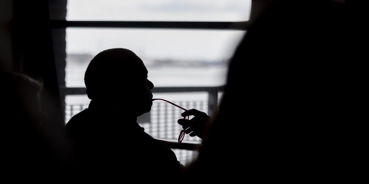 Silhouette of a person's profile pensively thinking while holding their glasses near their face.